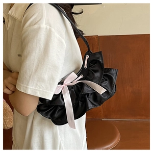 Detail of black pleated shoulder bag featuring a large pink silk bow and thin strap