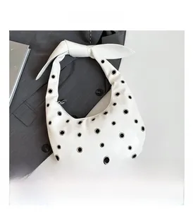 Macro view showing silver metal eyelets and knotted strap detail on white hobo bag