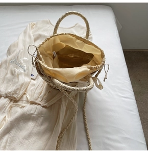 Overhead view of a woven straw bucket bag with drawstring liner on a white bed linen