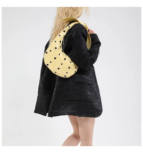 Detail of pale yellow patent leather crescent bag with silver oversized metal grommets