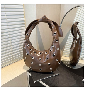 Detail of a brown hobo bag with silver grommets and a stylish knotted handle design