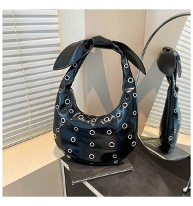 Detail of black patent leather hobo bag with silver eyelets and a large bow decoration