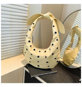 Detail of beige patent leather hobo bag with metal eyelets and knotted bow shoulder strap