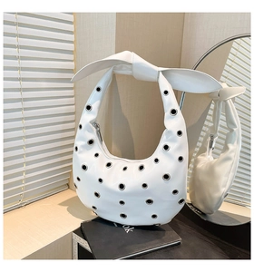 Detail of white leather crescent tote featuring silver eyelets and large bow shoulder strap