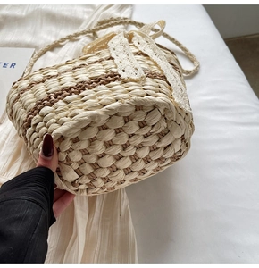 Detailed close-up of beige and brown woven straw bag with lace bow and hand strap