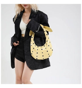 Detail showing pale yellow patent leather shoulder bag with silver eyelets and knot handle