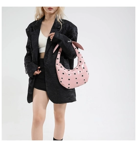 Close-up of pink crescent tote bag with metal grommets worn over a black blazer