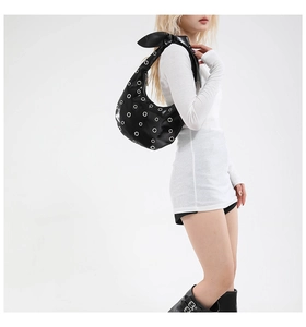 Detail of black crescent underarm bag with silver eyelets and large bow on shoulder strap