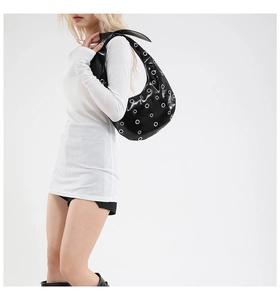 Detail of black glossy hobo bag with silver metal eyelets and wide shoulder strap