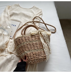 Detail of hand-woven straw bucket bag featuring a large cream lace bow on a beige dress