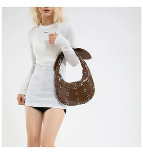 Detail of dark brown leather crescent bag with silver eyelets and knot strap detail