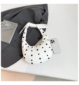Detailed top view of white hobo bag with metal eyelets and knotted strap on minimalist background