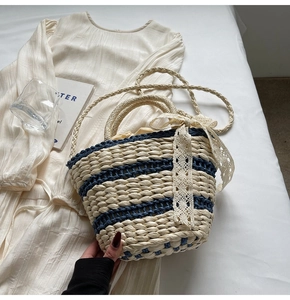 Detail of woven straw bucket bag featuring blue stripes and a white lace bow accent