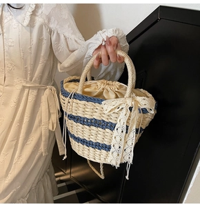 Detail of woven straw bucket bag with blue stripes and elegant white lace bow decoration