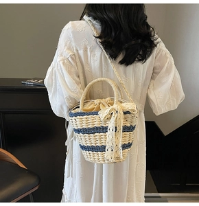 Detail of straw woven bag with blue stripes and lace bow on a model shoulder