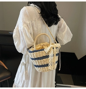 Detail of striped straw bucket bag featuring a cream lace bow and drawstring closure