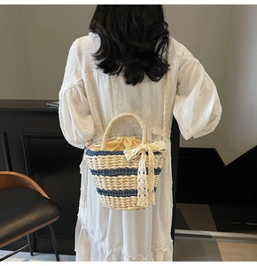 Detailed view of cream straw bucket bag featuring navy stripes and lace bow decoration