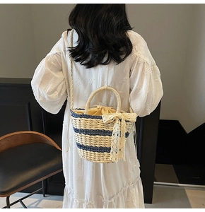 Detail of woven straw bucket bag with blue contrast trim and beige lace bow decoration