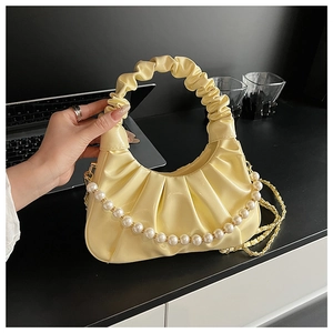 Detail view of yellow pleated cloud handbag with pearl chain and gold metal strap