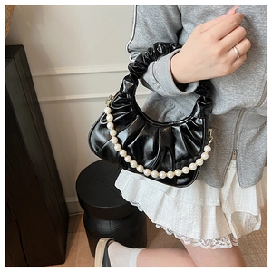 Detail of black pleated cloud bag featuring glossy leather and large pearl chain strap