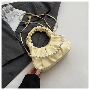 Detail of a beige pleated cloud bag featuring a large pearl handle and gold chain strap