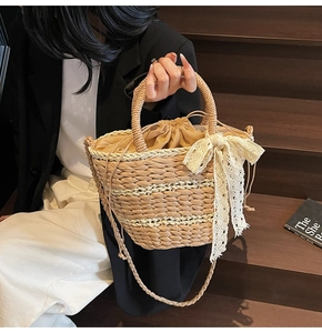 Detail of hand-woven straw bucket bag featuring a large lace bow and drawstring lining