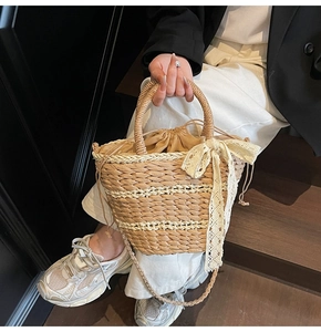 Detail of woven straw bucket bag with lace bow, drawstring closure and crossbody strap