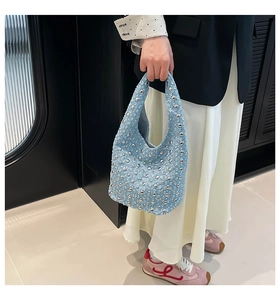 Close-up of light blue denim shoulder bag featuring silver metal rivet stud details