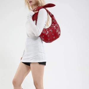 Red glossy crescent tote bag with silver eyelets and bow detail shown on a model