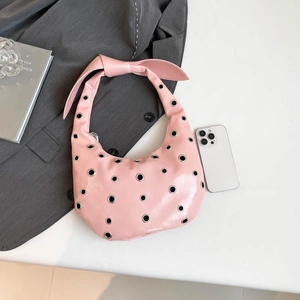 Pink patent leather hobo bag with silver eyelets and a bow handle on white background