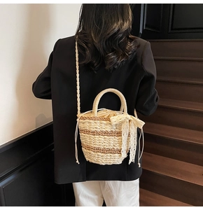 Detail of woven straw bucket bag showing lace bow and drawstring liner on a model