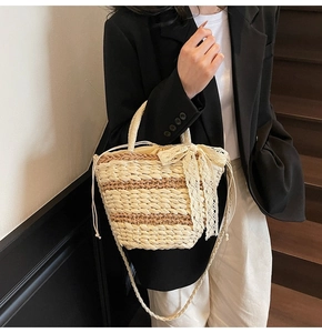 Detail of hand-woven straw bucket bag featuring a large cream lace bow and striped texture