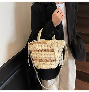 Detail of woven straw bucket bag with lace bow and drawstring liner in beige stripes