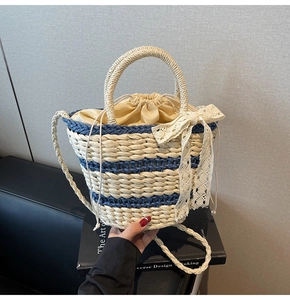 Detail of hand-woven straw bucket bag featuring blue stripes and a delicate lace bow accent