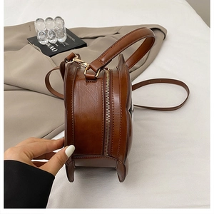 Side view of brown round vintage clock-shaped handbag with premium gold dual zippers