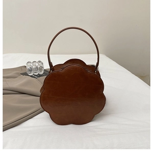 Detailed view of flower shaped dark brown handbag with textured faux leather on white fabric