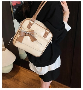 Detail of a beige shoulder bag featuring a large brown bow and silver ribbon accents
