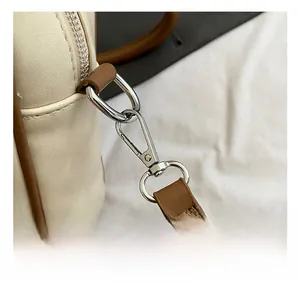 Close-up of durable silver metal hook and brown leather strap on cream shoulder bag