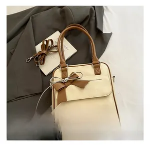 Detail of minimalist cream handbag featuring a brown bow accent and magnetic flap closure