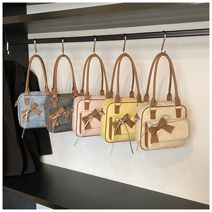 Five assorted colors of shoulder bags with bows and tassels hanging on a rack
