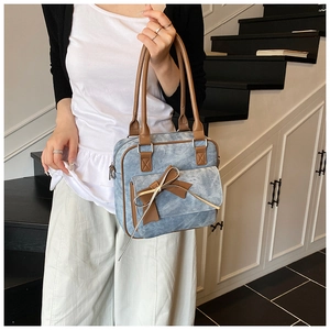 Detail of light blue denim handbag featuring a brown leather bow and metallic zipper