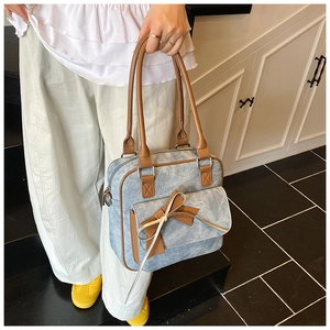 Detail of blue denim shoulder bag with brown leather trim and large decorative bow knot