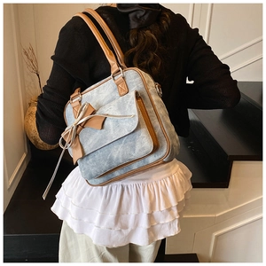 Detail of blue denim tote bag with brown leather trim and bow on model's shoulder