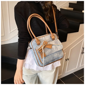 Detail of blue denim shoulder bag with brown leather trim and bow decoration
