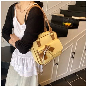 Detail of yellow leather shoulder bag featuring a vintage brown bow and silver ribbon