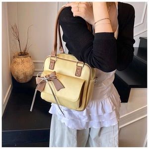 Detail of yellow leather shoulder bag with brown bow accent and contrast stitching