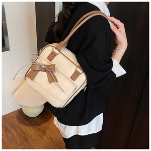 Detail of a cream shoulder bag featuring a large brown bow accent and a metal zipper closure