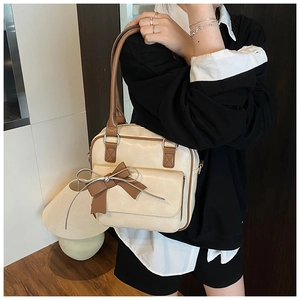 Close-up of beige shoulder bag featuring a large dark brown bow and sleek zipper detail