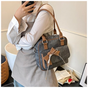 Detail of grey shoulder bag with brown leather handles and a bow decoration