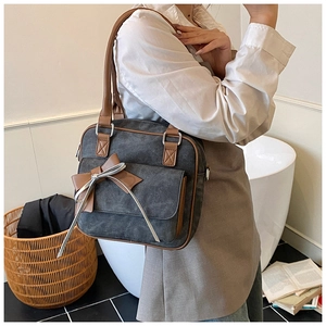 Detail of grey canvas shoulder bag with brown leather trim and stylish bow accent